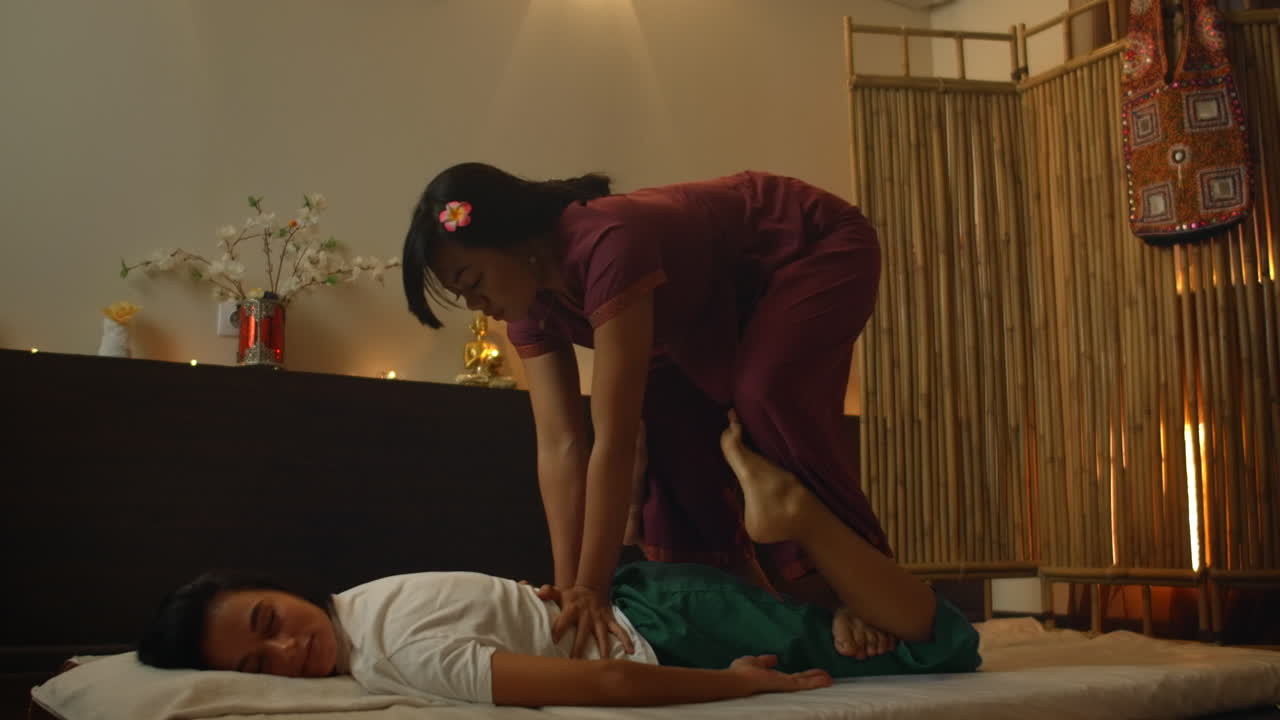 Alternative Chinese medicine an Asian woman performs therapeutic massage on the back and legs of a Caucasian woman lying on a couch. Aromatherapy and manual therapy by Chinese masters.