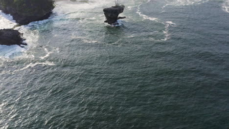 Small-boat-in-front-of-the-scenic-tropical-coastline-with-crashing-waves-at-the-stony-shore