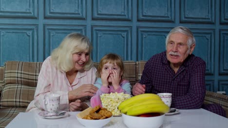 Family-grandparents-getting-scared-watching-horror-TV-television-movie-with-granddaughter-at-home