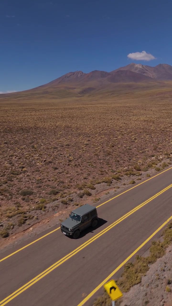 SUV compatto fuoristrada che percorre una strada asfaltata liscia attraverso il terreno accidentato del deserto di Atacama, tracciamento verticale con drone