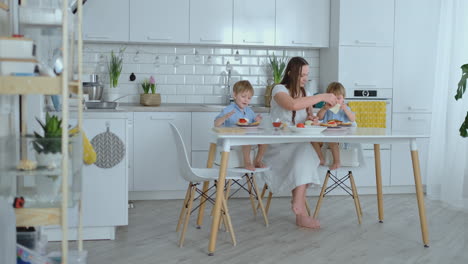 Young-mother-with-two-young-sons-in-the-kitchen-at-the-table-preparing-burger-for-lunch