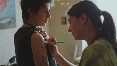 young woman talking with tattoo artist drawing stencil on her skin