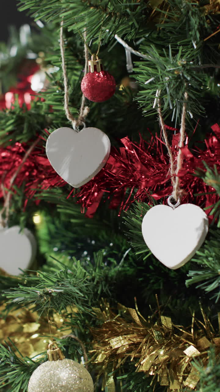 Vertical video of christmas tree with decorations and white hearts with copy space