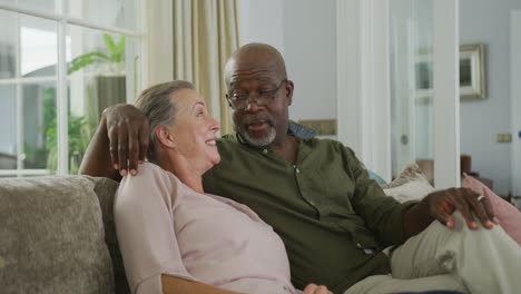 Feliz-Pareja-Diversa-De-Ancianos-Usando-Camisas-Y-Viendo-Televisión-En-La-Sala-De-Estar