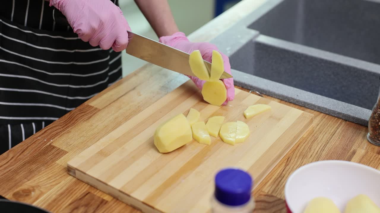 Person in pink gloves slicing potatoes on a wooden cutting board