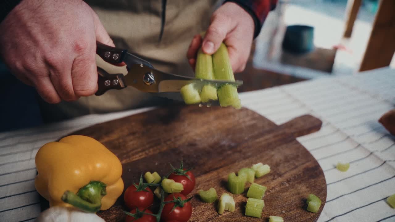 una persona corta apio fresco con tijeras en una tabla de madera, rodeada de verduras