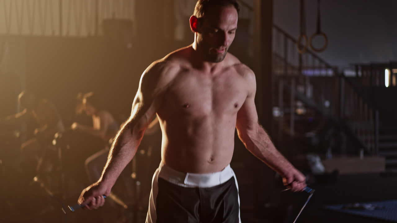 Shirtless man working out with a jump rope in a gym