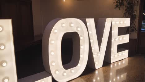 A close-up of giant, illuminated marquee letters spelling &quot;LOVE&quot; in a dark indoor space with a tiled floor