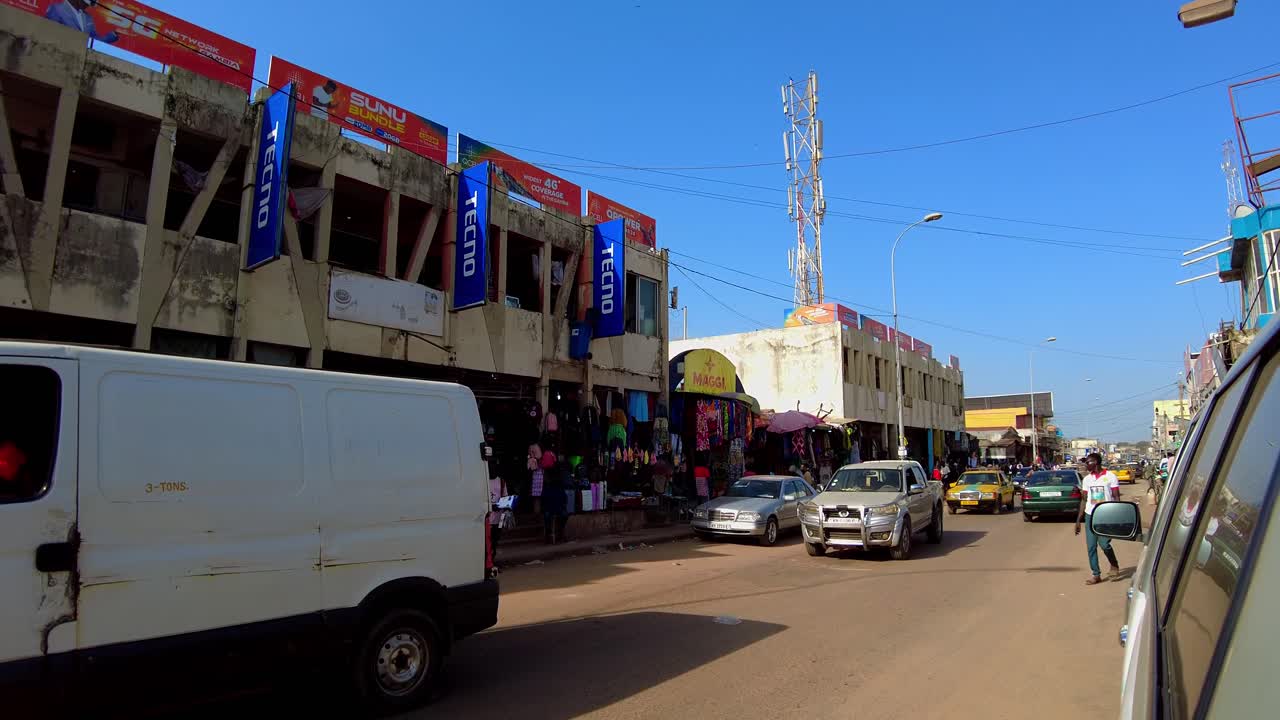 Pan shot capturing busy traffic at Serekunda Market street during busy hours on weekdays in Gambia.