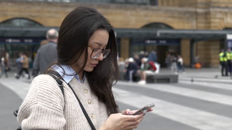 beautiful young woman stood outside train station on her smartphone