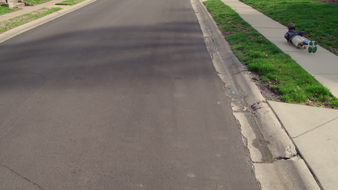 작은 소년이 스케이트보드 위에 배를 고 보행로를 타고 내려간다.