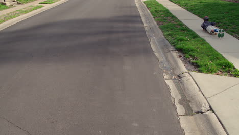 un niño pequeño viaja por la acera en su vientre en una patineta