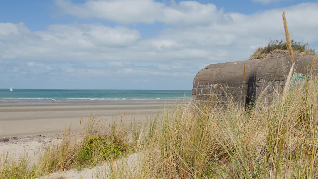 Historic concrete bunker amid sand dunes, calm seaside, bright daylight, wide static landscape shot