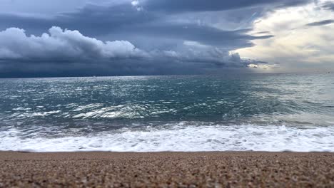 Mediterranean-beach-with-calm-water-coarse-sand-and-a-storm-in-the-background-dark-gray-black-sky
