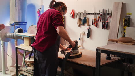 woodworking expert in carpentry shop using angle grinder to fix wooden surface