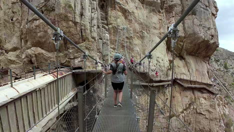 말라가의 아르달레스에 있는 카미니토 델 레이 (caminito del rey) 에 있는 가이타네스 (gaitanes) 협곡의 매달린 다리를 가로지르는 여자