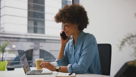 Mujer-De-Negocios-En-Una-Oficina-Moderna-Trabajando-En-Una-Computadora-Portátil-Y-Hablando-Por-Teléfono-Móvil