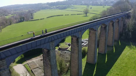 people walk across the beautiful narrow boat canal route called the pontcysyllte aqueduct famously designed by thomas telford, located in the beautiful welsh countryside, a huge bridge viaduct