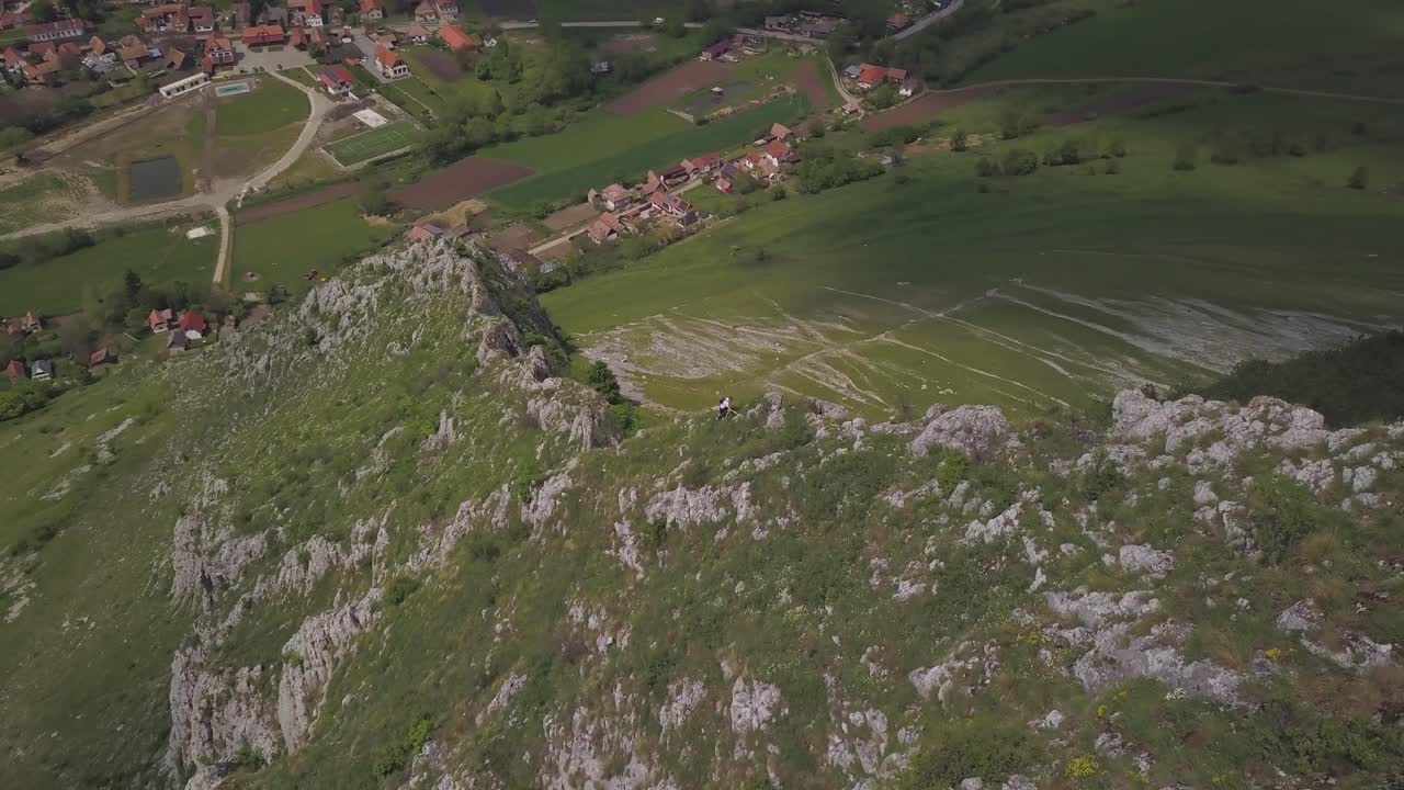 Aerial View From Above Of Hiker Climbing Rocky Mountain With Mountainside Green Valley Town Down