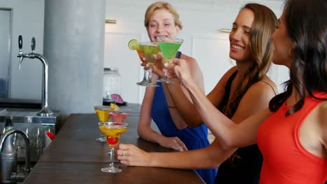 happy friends are sitting on counter and holding cocktail