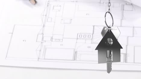 House-keys-and-key-fob-hanging-over-architectural-drawing-in-the-background