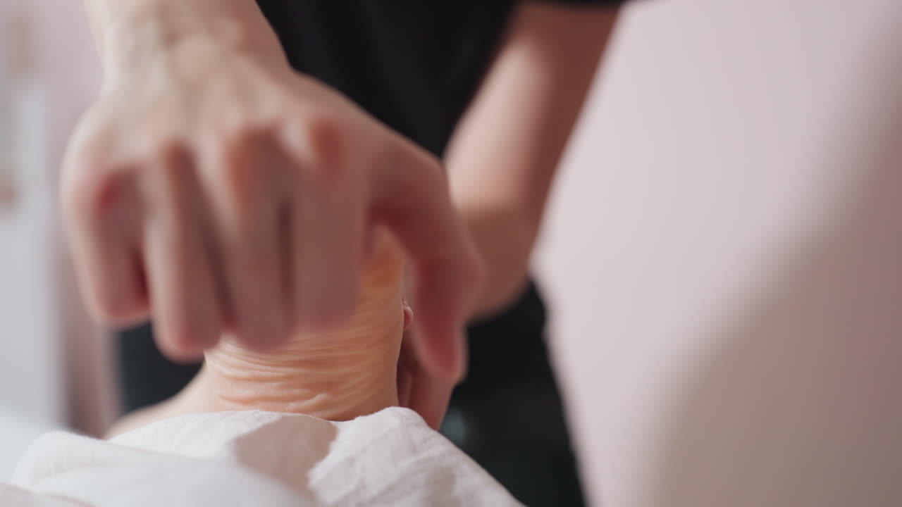 Close view of massage therapist gently massaging and stretching client foot using fingers, focus on toes and sole with visible skin spot, calm atmosphere during wellness therapy session