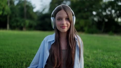 young woman wearing headphones and smiling in a park