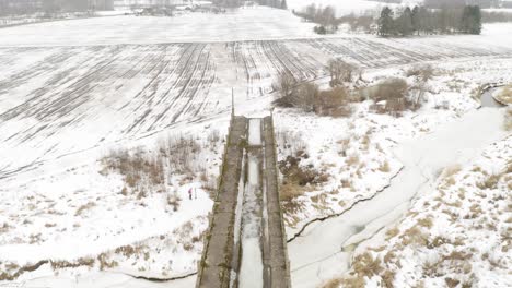 Aerial-view-of-abandoned-bridge-and-agricultural-field-during-winter