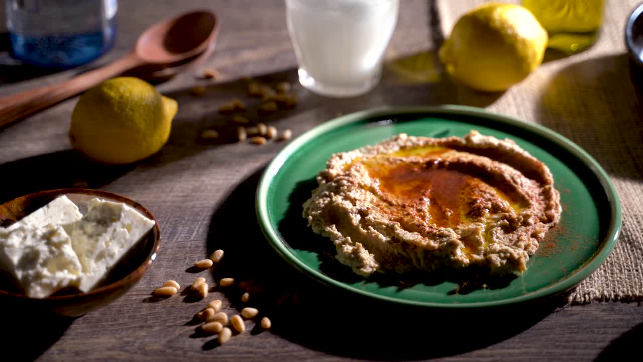 Contrasty, low angle slide to the left showing middle eastern food spread of olives, pine nuts, hummus, feta and ouzo