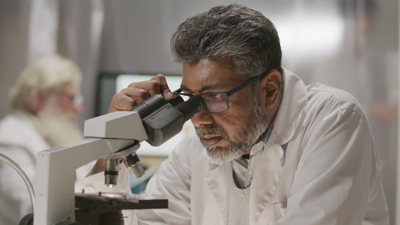 Scienziato maturo che conduce ricerche con il microscopio in un laboratorio di archeologia.