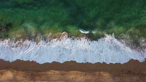 aerial top down view over clear, transparent ocean water foaming at the shore, washing the golden sand of the beach