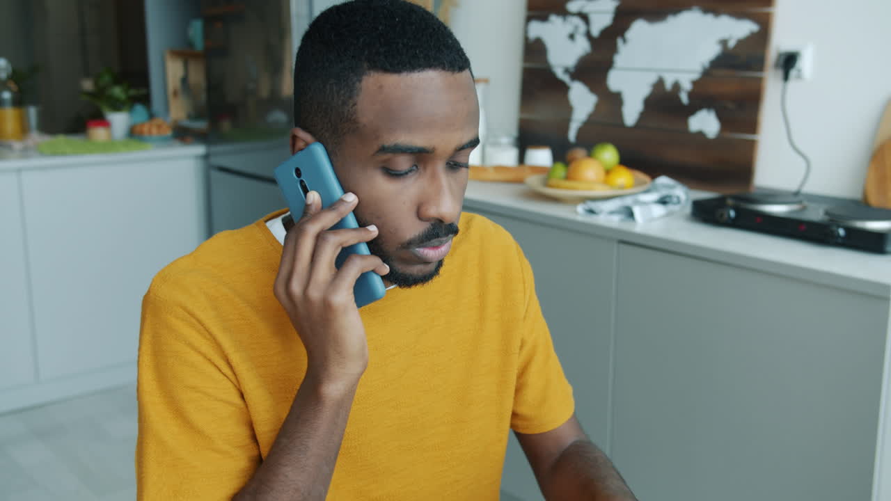 Man Talking on Phone and Working on Laptop in Kitchen