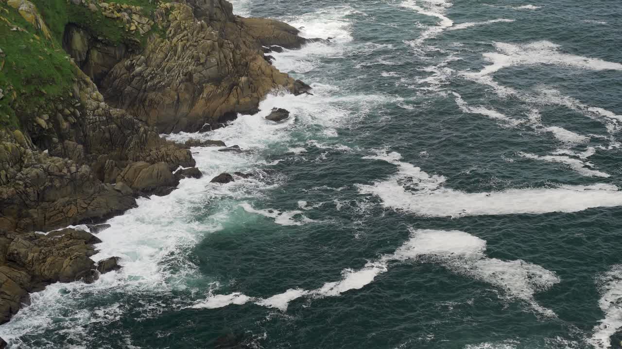 Shot from the top of a high cliff with the sea and the foamy waves crashing against the rocks