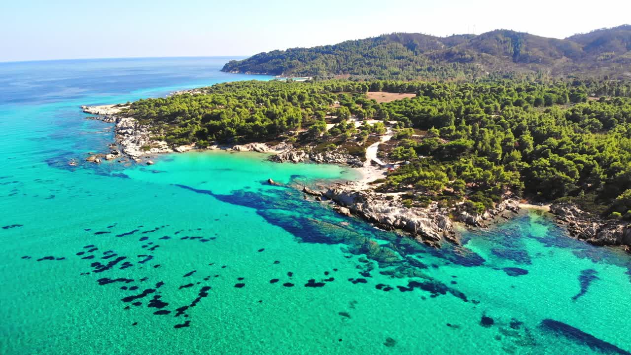 Vista aérea con dron de la costa rocosa del mar Egeo con agua azul transparente, vegetación variada y colinas. Grecia