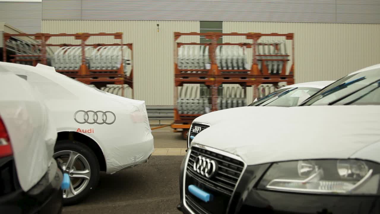 New Audi cars covered in protective sheets at a manufacturing plant with train with parts in the back