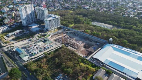 Orbiting-aerial-view-of-Philippine-city-construction-zone-and-large-crane-surrounded-by-trees-and-neighboring-buildings