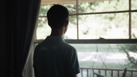 Young-man,-teenage-boy-looking-outside-window