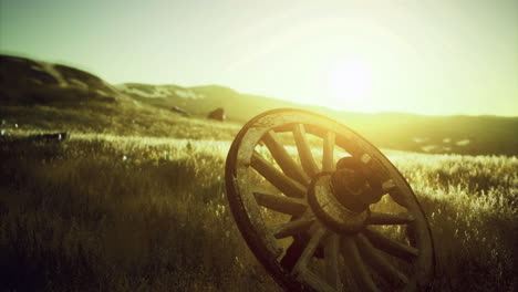 old wooden wagon wheel rests in a sunlit meadow with gentle hills