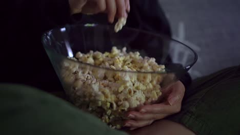 anonymous woman sitting on sofa and eating popcorn