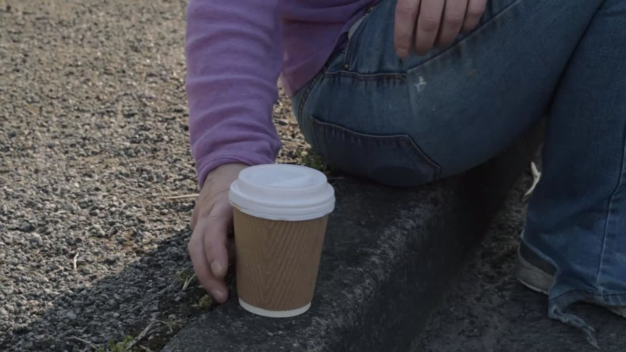 Sitting on the sidewalk drinking takeout coffee medium shot