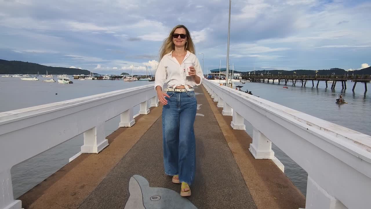 Mujer caminando en un muelle junto al océano con un café