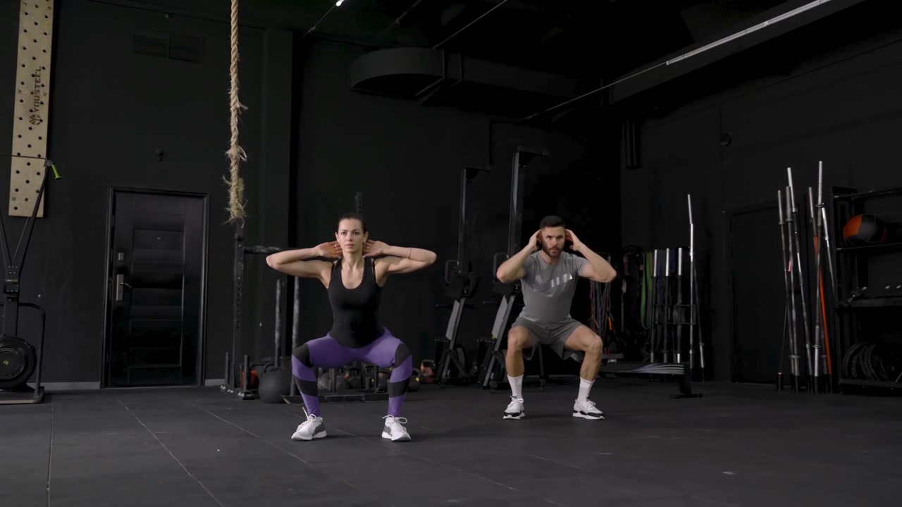 Uomo e Donna che Eseguono Squat in una Palestra Moderna