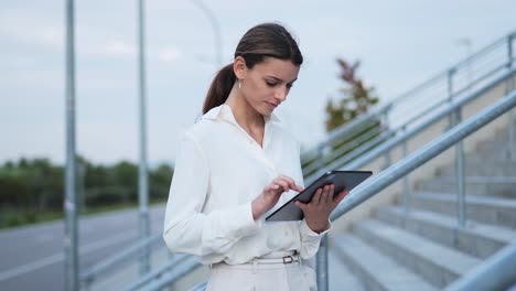 young-businesswoman-staying-on-the-stairs-while-working-on-her-tablet