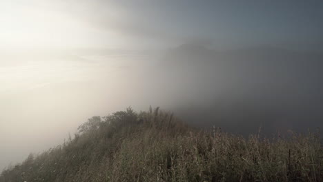 4K static shot view from a hill of dramatic and bright rolling clouds and fog moving fast and  hiding a mountain range in the distance