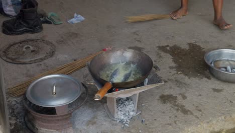 fry fish in a hot pan on a charcoal stove on the floor, an accompaniment to banku, a traditional ghanaian dumpling dish