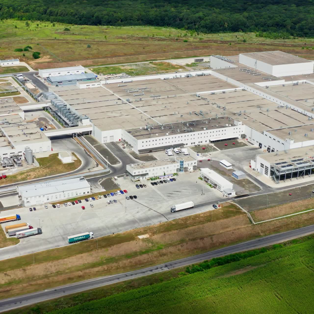 Industrial plant in green nature. Large area of contemporary factory with many trucks and parking places. Harmful manufacture in environment. Aerial view