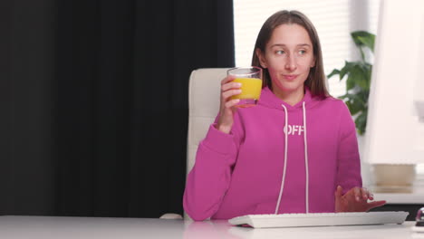 Mujer-Joven-Bebiendo-Un-Jugo-De-Naranja-Saludable-Mientras-Usa-Una-Computadora-De-Escritorio-En-La-Oficina-1