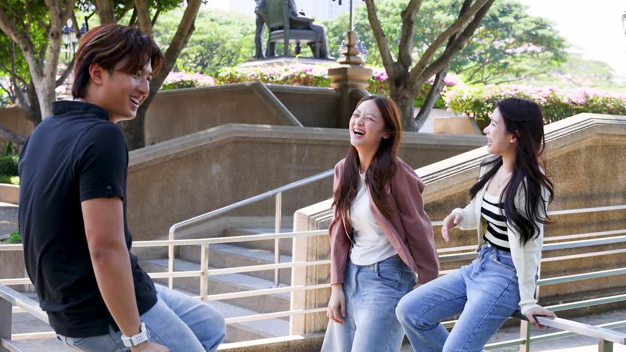 เพื่อนวัยหนุ่มสาวในชุดลำลองหัวเราะและพูดคุยกันกลางแจ้งในวิทยาเขตมหาวิทยาลัยที่มีแดดสดใส