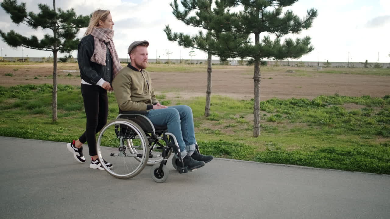 mujer empujando a un hombre en silla de ruedas a través de un parque