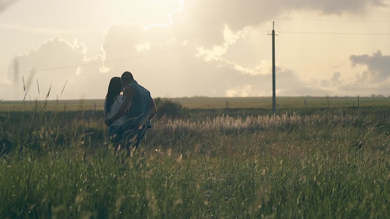 젊은 부부는 일몰 때 오렌지색 구름이 가득한 하늘 아래 춤을 춘다.